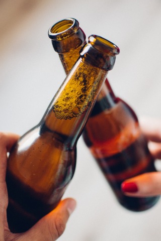 2 hands holding brown beer bottles clinking together